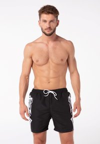 Čierne plavky s bielym kmeňovým vzorom na boku. Vyrobené z ľahkého materiálu, s elastickým pásom a šnúrkou na stiahnutie.