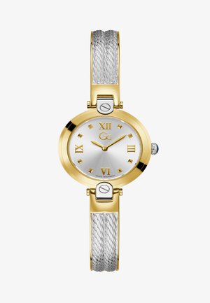 Kuldtooni kell, millel on hõbedane dial. Rooma numbrid ja teemantkujulised tunni markerid. Metallist käevõru keerduva hõbedase disainiga.