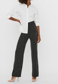 Pantalones grises de pierna ancha hechos de una suave tela de punto, combinados con una camiseta blanca de botones y tacones nude.