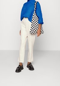 Blå stickad polotröja, krämfärgade skräddarsydda byxor, svarta kraftiga loafers och en svartvit rutad tote-väska.