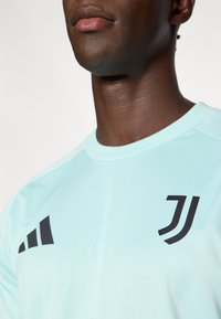 Light blue athletic shirt with black lettering and stripes on the left shoulder. Made from smooth, breathable fabric with a crew neckline.