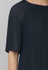 Robe plissée bleu marine foncé à manches courtes, présentant un tissu texturé et un col rond, mettant en valeur des lignes verticales et le mouvement.