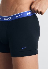 Schwarze Boxershorts mit einem blauen elastischen Bund, auf dem das "NIKE"-Logo abgebildet ist. Das Material wirkt glatt und hat ein enganliegendes Design mit minimalen Nähten.
