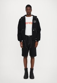 Black fleece hoodie with gray lining, white graphic t-shirt with pink lettering, black shorts with white stitching, and black ankle boots.
