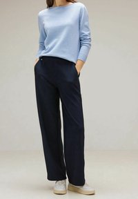 Ljusblå tröja med ribbade ärmar, kombinerad med mörkblå byxor med vida ben och ett randigt mönster samt sidofickor. Lätta vita sneakers.