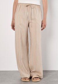 Pantalons larges à rayures beiges et blanches avec une taille élastique et un cordon de serrage. Tissu doux et léger avec une coupe décontractée.