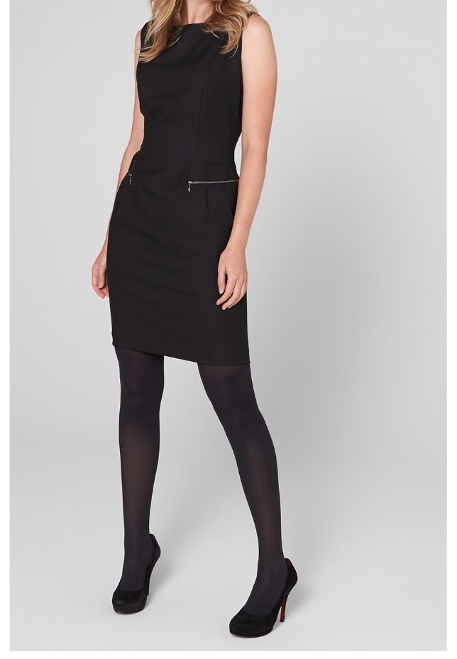 Svart ärmlös klänning i mjukt tyg, med två fickor med dragkedjor, en figursydd design och knälång skärning. Matchas med svarta strumpbyxor och klackar.