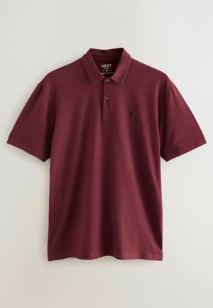 Burgundi polo särg klassikalise kraega, lühikeste varrukatega ja väikese musta logoga rinnas. Valmistatud pehmest puuvillast materjalist. Tavaline istuvus.