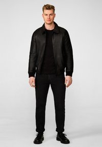 Black leather bomber jacket with ribbed cuffs and collar, worn over a black t-shirt, paired with black jeans and black shoes.
