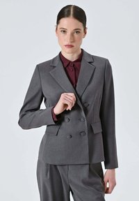 Blazer doppiopetto grigio in tessuto liscio simile alla lana con rever a lancia, due tasche frontali e dettagli con bottoni, indossato sopra una camicia bordeaux.