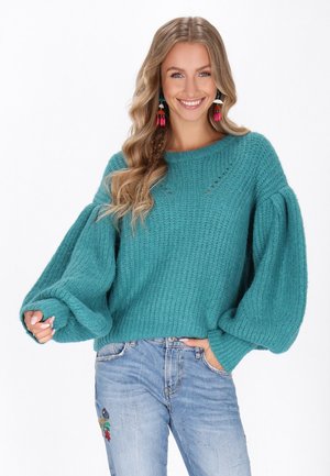 Pulover tricotat de culoare teal, cu manșoni balloon supradimensionați, prezentând o suprafață texturată și un decolteu rotund. Croială casual, asortat cu blugi decolorati.