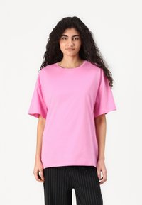 Rosa bomulls-t-skjorte med løs passform, rund hals og korte ermer, parret med svarte bukser med pinstriper. Glatt tekstur, enkelt design.