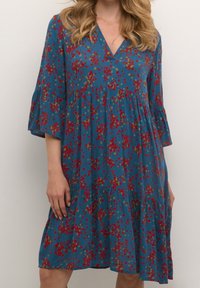 Robe fleurie bleue avec motifs rouges et verts, manches évasées et design à volants, en tissu léger avec un décolleté en V.