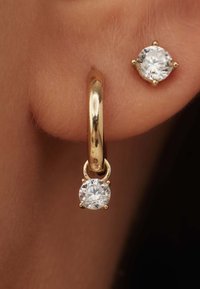Boucle d'oreille en or avec un cristal rond transparent suspendu amovible, accompagnée d'une boucle d'oreille puce avec un cristal rond plus petit.