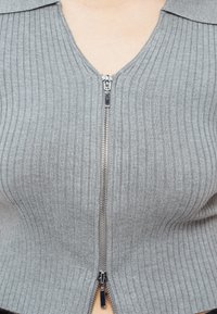 Κοντινό πλάνο ενός γκρι πλεκτού πουλόβερ με φερμουάρ και γιακά, μερικώς ανοιχτό από κάτω προς τα πάνω, αποκαλύπτοντας μια μικρή περιοχή δέρματος στο λαιμό.