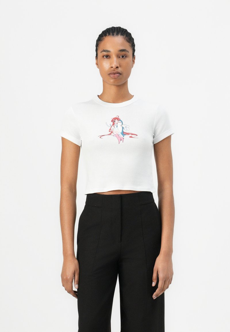 T-shirt blanc court à manches courtes avec un graphique de sirène coloré. Associé à un pantalon noir taille haute.