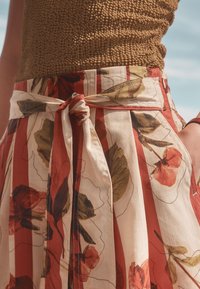 Jupe à motif floral avec des rayures rouges et crème, présentant un détail de taille nouée, des plis et une texture de tissu léger.