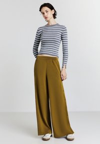Top en tricot à rayures à manches longues en gris et blanc, associé à un pantalon large jaune moutarde avec des boutons sur le côté et un tissu doux et texturé.