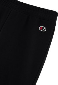 Pantalon de survêtement noir en tissu mélangé de coton, doté d'une taille élastique et d'un petit logo brodé en rouge et blanc sur le côté gauche.