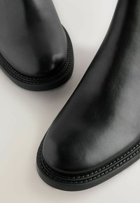Czarne botki za kostkę wykonane z gładkiej skóry, z okrągłym noskiem i dekoracyjnym przeszyciem wzdłuż podeszwy. Minimalistyczny i elegancki design.