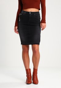 Svart jeanstyg blyertkjol med fransade kanter, hög midja och framfickor. Bärs med en rostfärgad långärmad topp och bruna anklarstövlar.