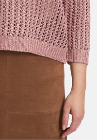 Jasnoróżowy sweter robiony na drutach z otwartym splotem, teksturowanym dołem i rękawami o długości trzech czwartych, zestawiony z brązową zamszową spódnicą.