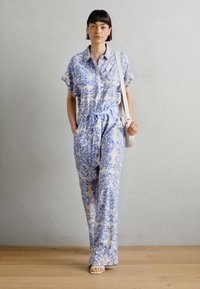 Kergest jumpsuit kreemjas värvikes koos sinise lillemustriga, lühikesed varrukad, nupuga esikülg, elastne vöökoht ja laiad, voolavad püksid.