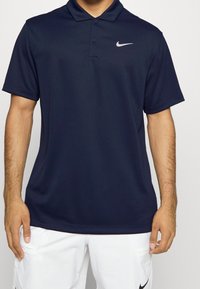Polo marine en tissu lisse, avec un col, des manches courtes et un petit logo Nike blanc sur la poitrine gauche.