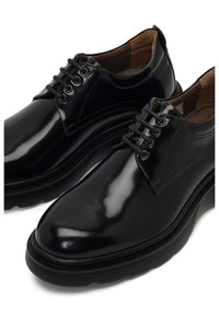 Chaussures en cuir noir avec une finition brillante, bout rond, design traditionnel à lacets et semelles texturées pour une adhérence et une stabilité accrues.
