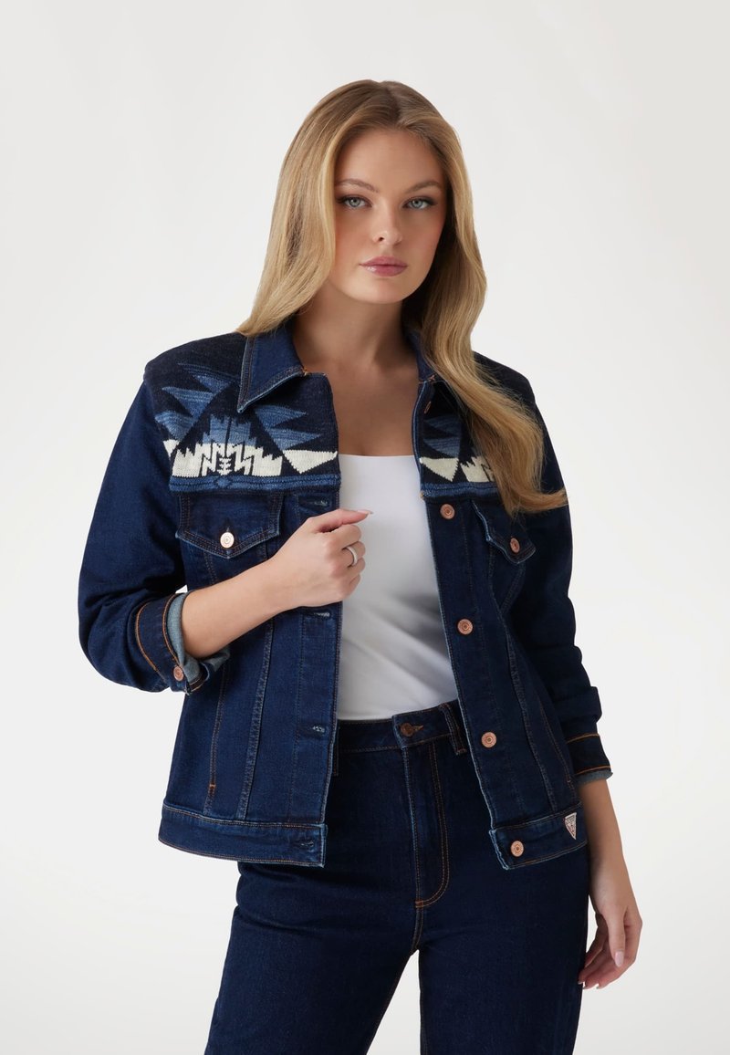 Tamsiai džinsinis švarkas su geometriniu audinių raštu ant pečių, su vario furnitūra, sagomis ir šiek tiek prigludusia forma.