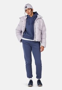 Jasnolila kurtka puchowa, granatowa bluza z kapturem i pasujące spodnie. Do cech należy zamki błyskawiczne, sznurki i tekstury w tkaninie. Sneakersy w kolorze ciemnoniebieskim.