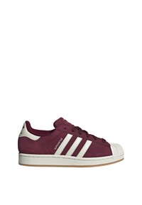 Maroon suede sneaker with white rubber shell toe and three white stripes. Lace-up design with a textured sole for grip.