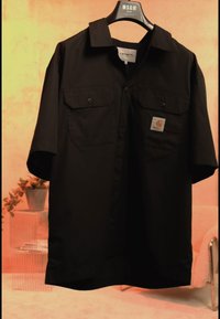 Zwarte korte mouwen blouse met knopen en twee borstzakken, waarvan één met een Carhartt-logo, hangend aan een MSGM-kledinghanger.