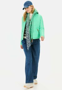 Lys grøn quilted jakke, marineblå tørklæde med blomstermønster, cremefarvet sweater, blå denim jeans og hvide sneakers med brune såler.