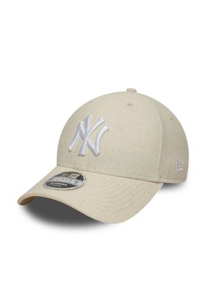 Beige honkbalpet met wit geborduurd New York Yankees-logo en een gebogen klep, afgebeeld tegen een witte achtergrond.