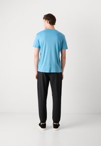 Hellblaues T-Shirt mit kurzen Ärmeln, schwarze eng anliegende Hose und schwarze Schuhe mit weißen Sohlen. Glatter Stoff, lässiger Schnitt und elastische Bündchen.