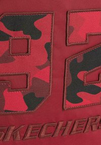 Tejido rojo con grandes números de camuflaje en negro y rojo "92" con costura texturizada y "SKECHERS" bordado en la parte inferior.