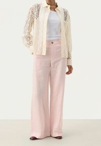 Hedvábná košile na knoflíčky v krémové barvě, spojená s světle růžovými lněnými kalhotami širokého střihu a hnědými lodičkami na podpatku. Má diamantové vzory a čistý siluetu.