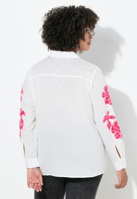 Weißes Hemd mit langen Ärmeln, pinkfarbenen floralem Stickerei an jedem Ärmel, seitliche Schlitze an den Manschetten, geknöpfte Manschetten, glattes Baumwollgewebe.