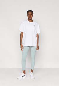 T-shirt blanc en coton surdimensionné avec logo noir, associé à des leggings vert menthe et des chaussures de sport blanches avec des rayures noires.