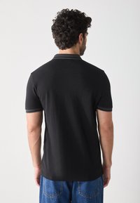 Schwarzes Poloshirt mit schlanker Passform, kurzärmelig und mit kontrastierendem Kragen. Glattes Material ohne sichtbare Muster oder Hardwaredetails.