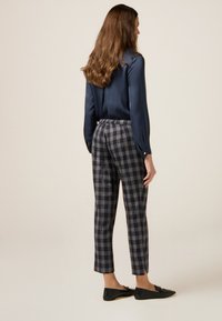 Granatowa bluzka z długimi rękawami, w zestawieniu z kraciastymi spodniami w odcieniach granatu i szarości. Spodnie mają zwężany kształt i boczne rozcięcia. Czarne płaskie buty.