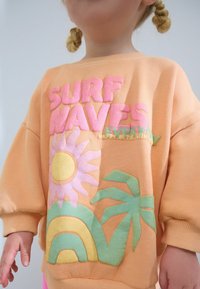 Sudadera melocotón con grandes gráficos texturizados en tonos pastel de un sol, una flor, una palmera y un arcoíris. Puños acanalados y cuello redondo.