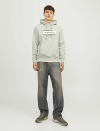 Jasnoszara bluza z kapturem z logo z przodu, regulowany kaptur, kieszeń kangurzą, zestawiona z niebieskimi, luźnymi dżinsami i szarymi trampkami.