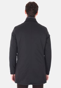 Cappotto imbottito nero con colletto alto, maniche lunghe, taglio dritto e superficie liscia, caratterizzato da un design pulito e minimalista.