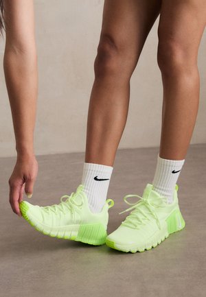 Neon green athletic shoes with textured sole, lace-up design, and a white Nike logo on the side. Worn with white socks featuring black accents.