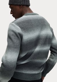 Maglione grigio con un motivo strutturato a coste. Presenta una sfumatura da grigio scuro a grigio chiaro, scollatura rotonda e maniche lunghe.