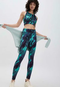 Twee-delig activewear set met een abstract patroon in teal en donkerblauw. De cropped top heeft een halternek; de legging heeft een hoge taille.