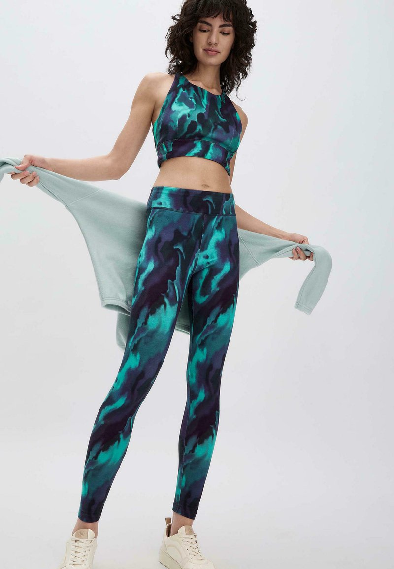 Twee-delig activewear set met een abstract patroon in teal en donkerblauw. De cropped top heeft een halternek; de legging heeft een hoge taille.