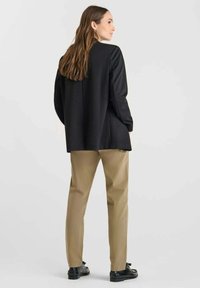 Veste noire ajustée sur un pantalon crème, avec une coupe décontractée, un design minimaliste et une texture lisse. Des chaussures noires complètent la tenue.